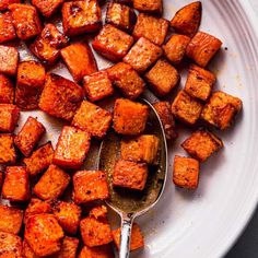 a white plate topped with sweet potatoes and a spoon next to it on top of a table