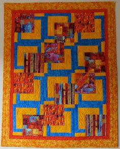 a quilted wall hanging on the side of a wall with orange, yellow and blue squares