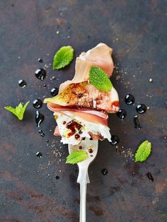 a spoon with some food on it sitting next to black olives and mint leaves