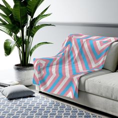 a pink and blue blanket sitting on top of a couch next to a potted plant