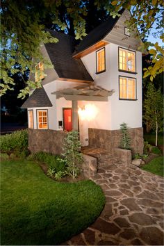 a small white house with red door and windows at night in front of some trees