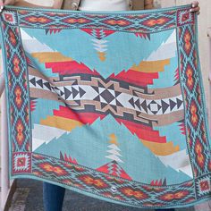 a woman holding up a colorful blanket with an arrow design on the front and back