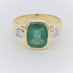 an emerald and diamond ring with three diamonds on the bottom, set in yellow gold