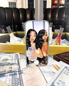 two beautiful women taking a selfie in a mirror with money and bottles behind them