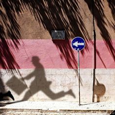 the shadow of a running man is cast on a wall next to a street sign