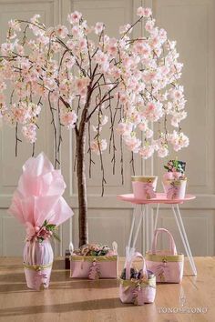 a tree with pink flowers and purses in front of it on a wooden table