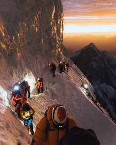 a group of people climbing up the side of a snow covered mountain at night time