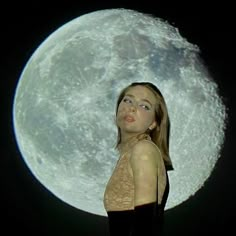 a woman standing in front of a full moon with her eyes closed and head tilted to the side