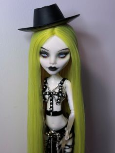 a doll with long green hair wearing a black top hat and silver chains on it's head