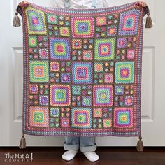 a woman holding up a colorful crocheted blanket