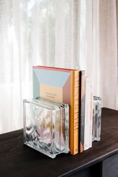 two books are stacked on top of each other near a glass vase and bookend