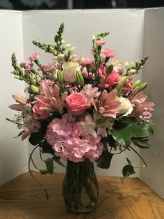 a vase filled with lots of pink flowers on top of a wooden table next to a white wall