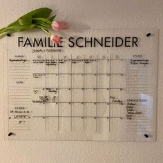 a family calendar hanging on the wall with flowers in it's center and one pink tulip resting on top