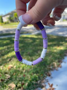 a person holding a purple and white beaded bracelet in their hand on the grass