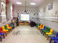 a classroom filled with lots of colorful chairs next to a projector screen on the wall