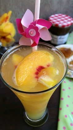 an orange drink in a glass with a pink flower on the top and some other desserts behind it