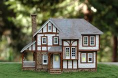 a model house sitting on top of a lush green field with trees in the background