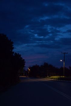 an empty street at night with the lights on and dark clouds in the sky above