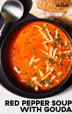 a bowl of red pepper soup with bread on the side