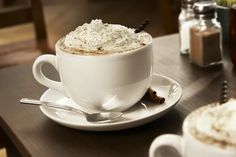 a cappuccino sits on a saucer next to a cup of coffee