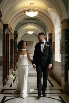 a bride and groom holding hands walking down the hall at their wedding reception in an old building