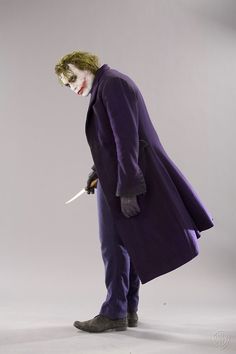 a man dressed as the joker holding a knife in one hand and wearing a purple coat