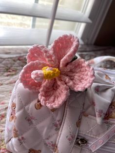 a crocheted pink flower sits on top of a white handbag in front of a window