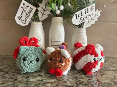 three small crocheted animals sitting next to each other on a counter top near vases with flowers in them