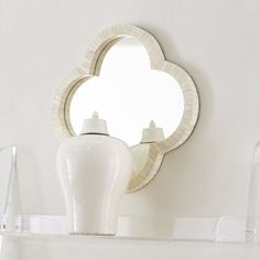 a white vase sitting on top of a shelf next to a mirror and light fixture