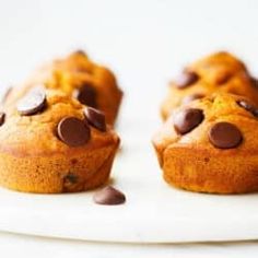 two chocolate chip muffins on a white plate with scattered chocolate chips around them