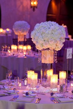 the centerpieces on this table are filled with white flowers and lit up candles