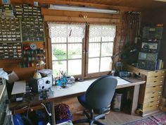 an office with lots of crafting supplies on the desk and in front of two windows