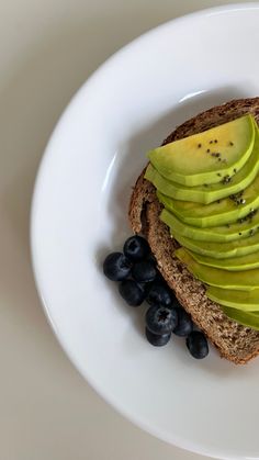 an open face sandwich with avocado and blueberries on a white platter