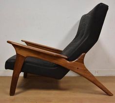 a black leather reclining chair with wooden legs and arm rests against a white wall