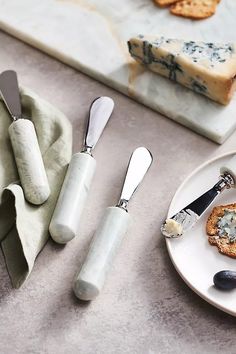 two cheese knives and some crackers on a white plate next to other food items