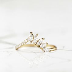 a gold ring with three pear shaped diamonds on the front and side, sitting on a white surface