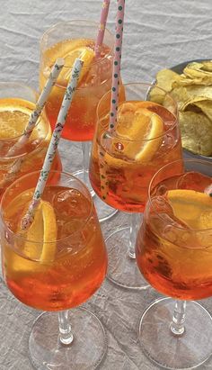 four glasses filled with orange juice and lemon slices on a table next to chips, crackers and strawberries