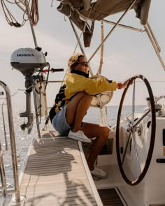 a woman sitting on the deck of a sailboat with her steering wheel in front of her