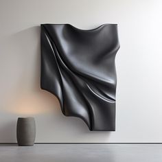 an abstract black sculpture next to a white vase on the floor in front of a wall