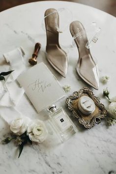 a table topped with white flowers next to a pair of high heeled shoes and perfume