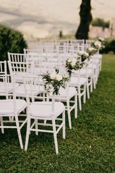 rows of white chairs with flowers on them are set up in the grass for an outdoor ceremony