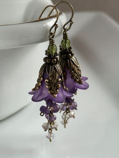 "Rich purple lily blossoms wearing a mantle of vintage-style antique brass caps, cascade a waterfall of tiny natural amethyst. These romantic earrings swing from antique brass French earwires or an earwire of your choice. Leverbacks, kidney wires, posts and non-pierced clips are available.  Please make your selection from the drop-down menu. All Debra Dane jewelry arrives in a pretty box suitable for gifting. 1.5\" (38mm)from bottom loop of earwire." Vintage Floral Jewelry, Whimsigoth Earrings, Cascade Earrings, Plant Earrings, Purple Lily, Purple Accessories, Amethyst Flower, Gift For Gardener, Romantic Earrings