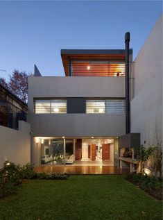 an exterior view of a modern house with grass in the front yard and lights on