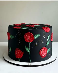 a black cake with red roses painted on the side and green leaves in the middle