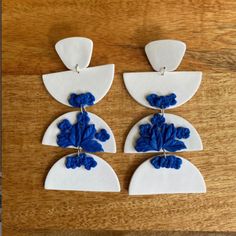 three white and blue earrings with flowers on them sitting on top of a wooden table