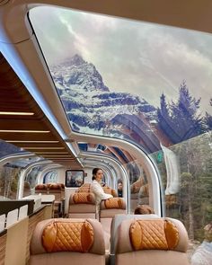 the interior of a train car with mountains in the background and people sitting on seats