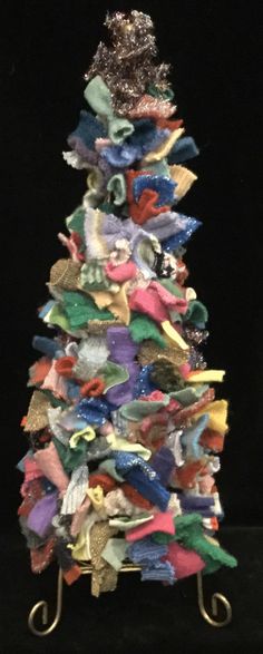 a small christmas tree made out of cloths on a metal stand in front of a black background