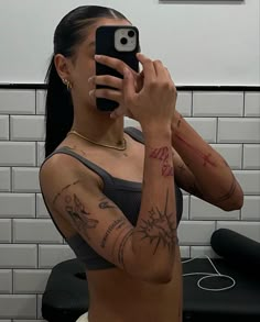 a woman taking a selfie with her cell phone in a bathroom mirror, wearing tattoos on her arm