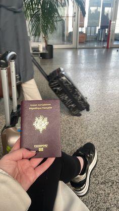 a person holding a passport in their hand at an airport with other luggage behind them