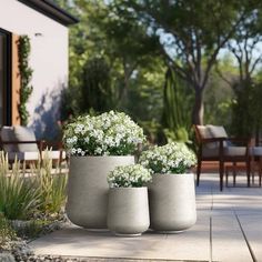 three cement planters with white flowers in them on a patio next to a table and chairs